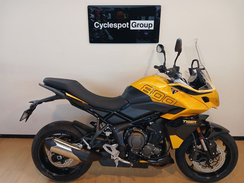 Load image into Gallery viewer, A yellow and black Triumph Tiger 800motorcycle is parked indoors against a light beige wall, with a 'Cyclespot Group' sign visible above it.