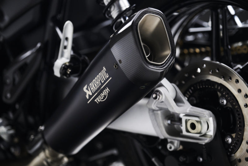 Load image into Gallery viewer, A close-up of a black Akrapovic Triumph motorcycle exhaust muffler mounted on a motorcycle, showing the brand logos and the metallic exhaust tip.
