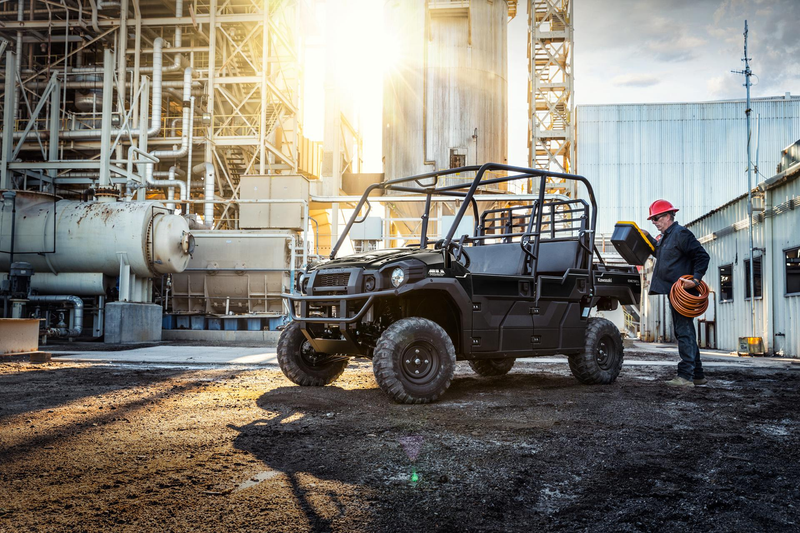 Load image into Gallery viewer, An all-terrain vehicle is parked on a dirt lot next to a white industrial building, with a man in a red hard hat standing nearby holding a yellow item. The scene is backlit by bright sunlight, casting strong shadows.