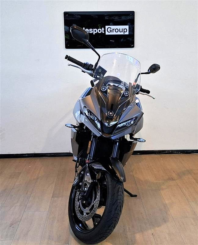 Load image into Gallery viewer, A grey 2023 Triumph Tiger Sport 660 motorcycle is parked indoors on a wooden floor against a white wall, with a 'spot Group' sign visible above it.