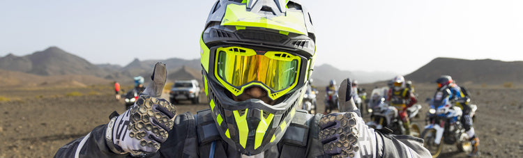 A rider wearing a hi-vis LS2 adventure motorcycle helmet and goggles giving a double thumbs up on an off-road tour.