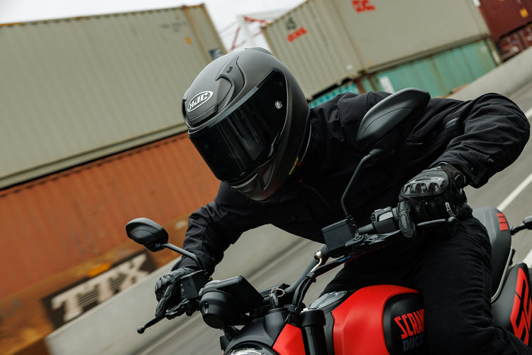 A rider wearing a matte black HJC RPHA 71 helmet and Alpinestars gloves on a red Ducati Scrambler, available at Cyclespot stores in Auckland, Taranaki, and Wellington