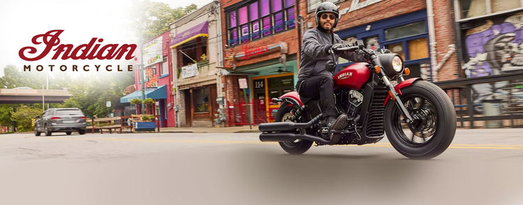 Indian Scout Rogue featuring blacked-out styling and a solo seat, riding through a colourful city street with the Indian Motorcycle logo.