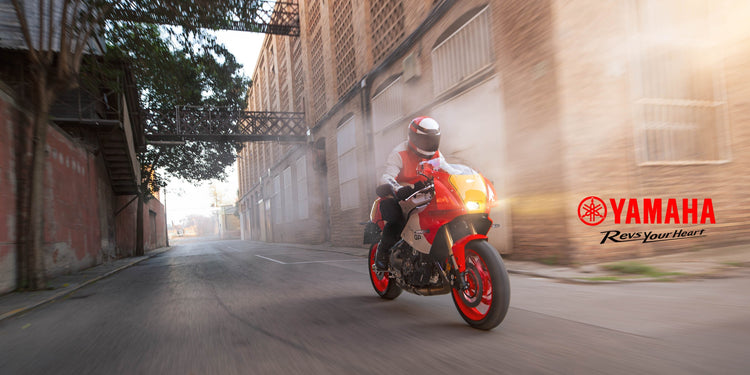 New Yamaha XSR900 GP sport motorcycle available at Cyclespot New Zealand, shown riding through an urban landscape with retro red and white styling.