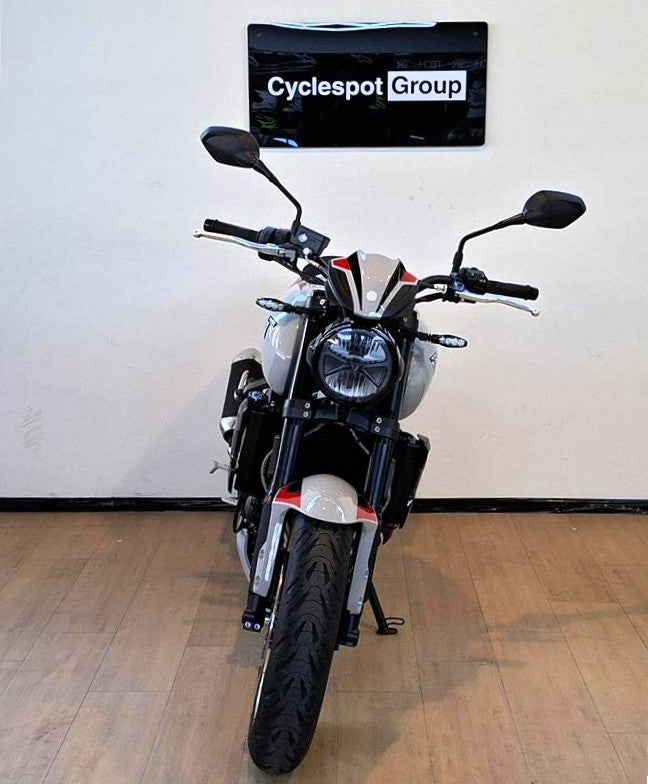 Load image into Gallery viewer, A black and silver Triumph Trident cruiser motorcycle with red accents, photographed from the front in a showroom with a wood floor and a wall sign reading 'Cyclespot Group'.

