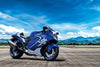 A blue and white 2026 Suzuki Hayabusa GSX 1300 RR Special Edition motorcycle parked on an open paved area with mountains and a bright blue sky in the background.