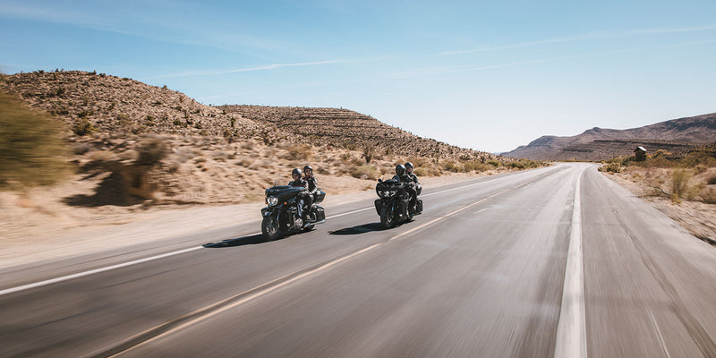 Load image into Gallery viewer, Two 2026 Indian Roadmaster Limited motorcycles travel side by side on a paved desert highway with rocky hills and a clear blue sky.
