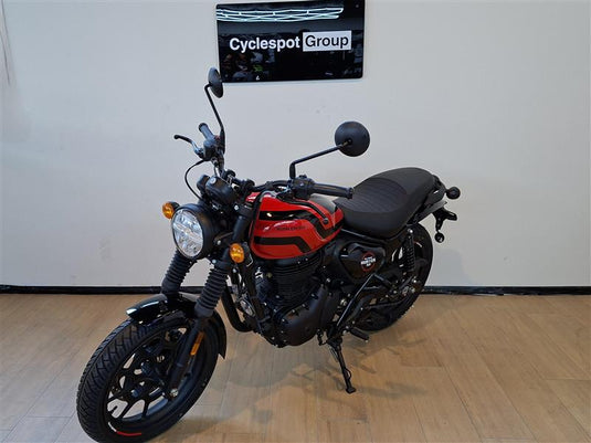 A red and black street motorcycle displayed indoors on a wooden floor against a white wall, with a visible 'Cyclespot Group' sign on the wall behind it.