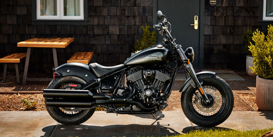 Black motorcycle parked outside a building with wooden tables and plants.