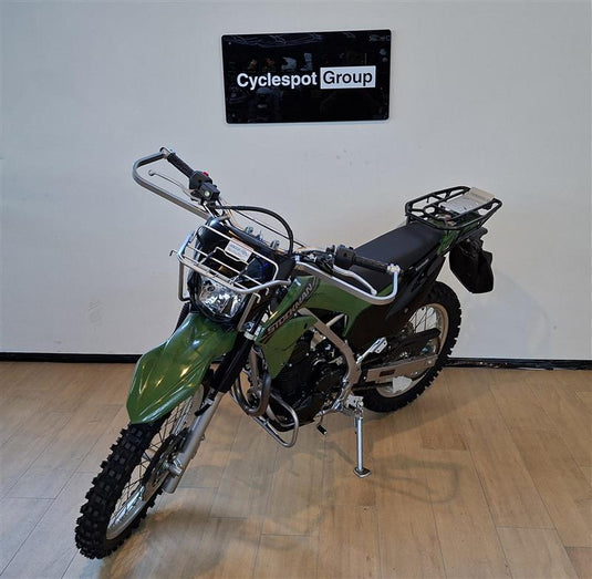 A green and black Stockman off-road motorcycle with a rear luggage rack, displayed on a wooden floor against a white wall with a 'Cyclespot Group' sign.