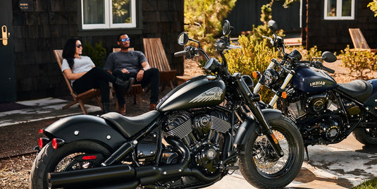 Two motorcycles parked outdoors with people sitting in the background.