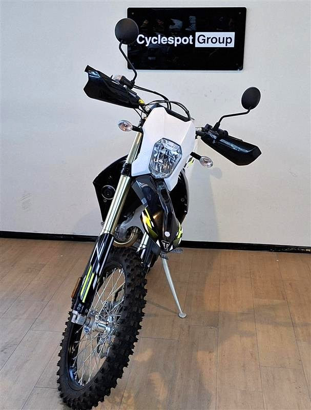 Load image into Gallery viewer, A Triumph TF 450-E dirt bike with a white front panel and black bodywork, displayed on a kickstand in a showroom with a wood floor and a 'Cyclespot Group' sign on the wall.
