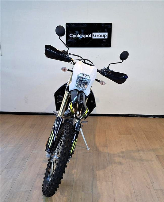 A black and white Triumph TF 250 E motorcycle with yellow accents, displayed on a kickstand in an indoor showroom with a wood floor and a wall sign reading 'Cyclespot Group'.