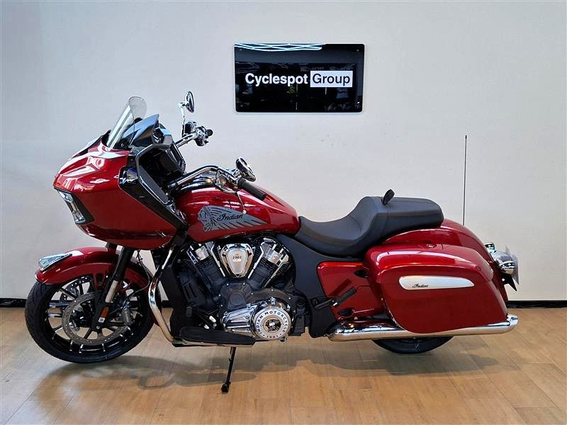Load image into Gallery viewer, A red and black Indian Challenger motorcycle is parked indoors on a wooden floor against a light gray wall, with a 'Cyclespot Group' sign visible on the wall behind it.
