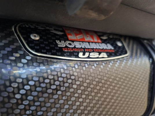 Close-up of a carbon fiber textured panel with a metallic badge reading Yoshimura Research and Development USA.
