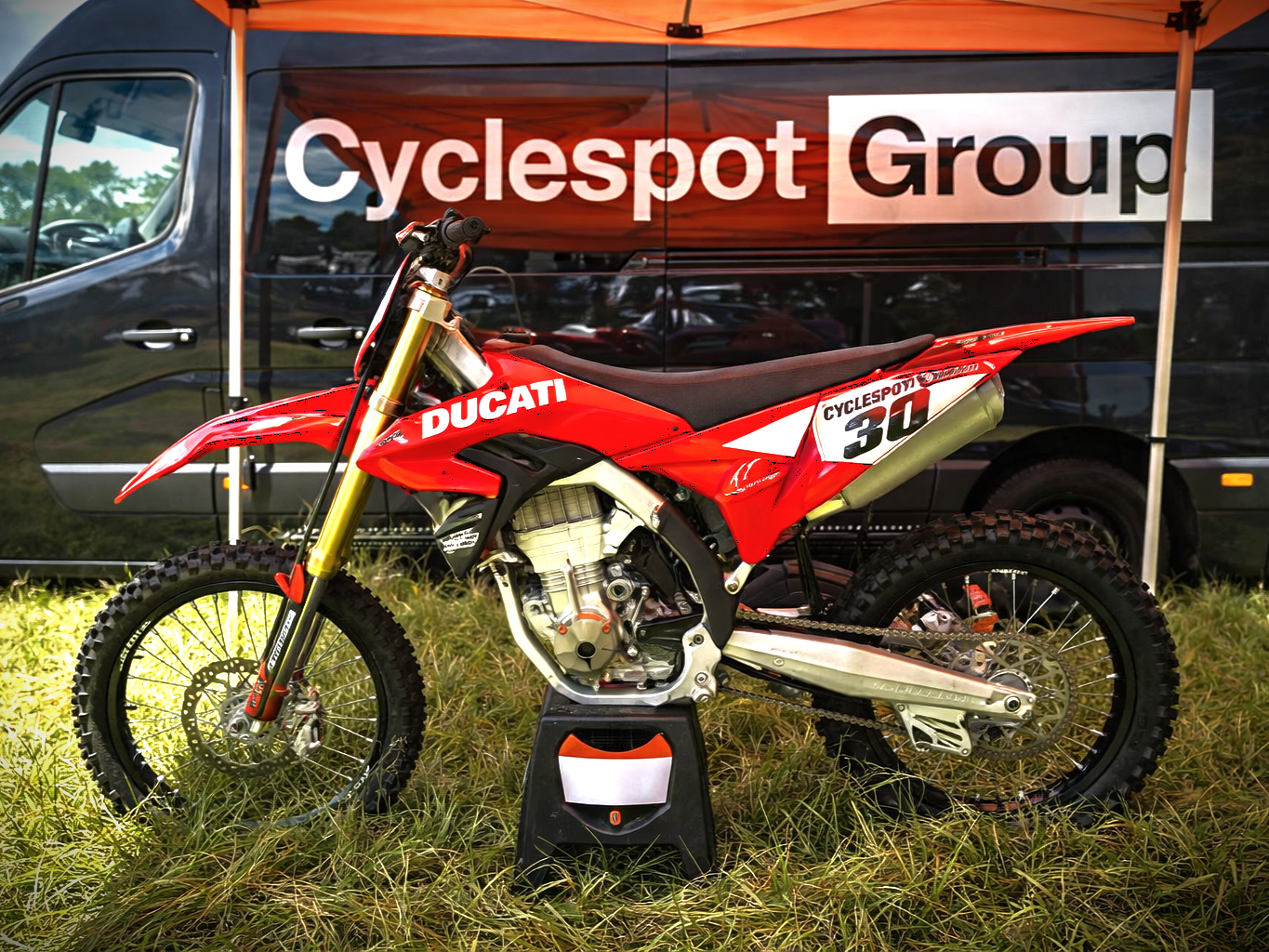Red Ducati dirt bike race motorcycle on display under a Cyclespot Group tent.