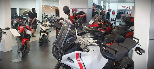 Showroom view at Cyclespot Wellington featuring a close-up of a white and red Ducati DesertX in the foreground, with various other Ducati models and branded riding apparel displayed throughout the modern dealership interior.