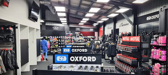 Interior of the Cyclespot Wellington showroom featuring organized retail displays of motorcycle apparel and accessories, including Oxford and Motul branded products, Shoei and HJC helmets, and Alpinestars riding gear under bright overhead lighting.