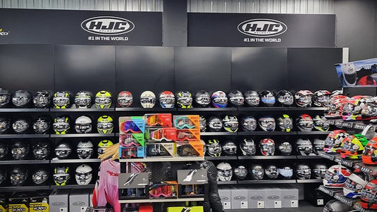 A retail display at Cyclespot Wellington featuring a comprehensive wall of HJC motorcycle helmets in various colours and styles, alongside shelves of 100% brand goggles and other protective riding gear.