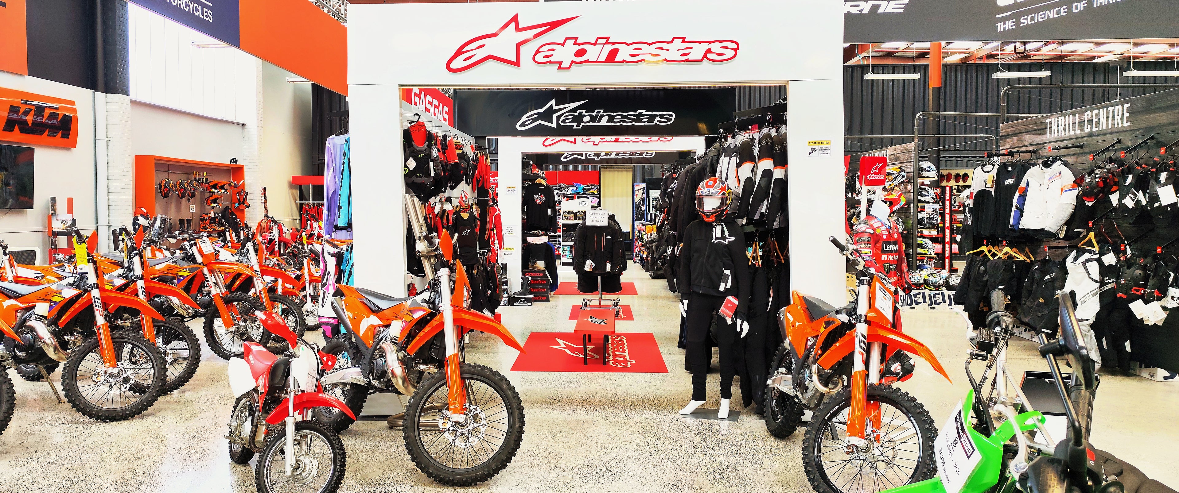 Interior of huge Cyclespot motorcycle showroom featuring the Alpinestars premium riding gear section, KTM dirt bikes, and a wide selection of helmets and apparel.