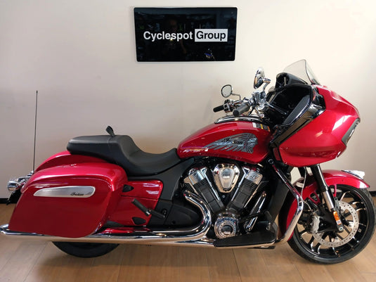 A red and black Indian Challenger Ltd motorcycle is parked indoors against a beige wall with a 'Cyclespot Group' sign above it. The bike features a large windscreen, saddlebags, chrome exhausts, and a V-twin engine.