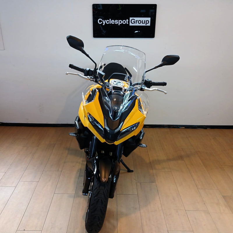Load image into Gallery viewer, A yellow and black Triumph Tiger 800 motorcycle with a clear windshield is parked indoors on a light wood floor against a white wall, with a sign reading 'Cyclespot Group' above it.
