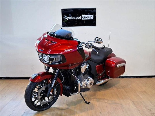 A red and black Indian Challenger Ltd touring motorcycle is parked indoors on a light wood floor against a white wall, with a sign reading 'Cyclespot Group' above it.