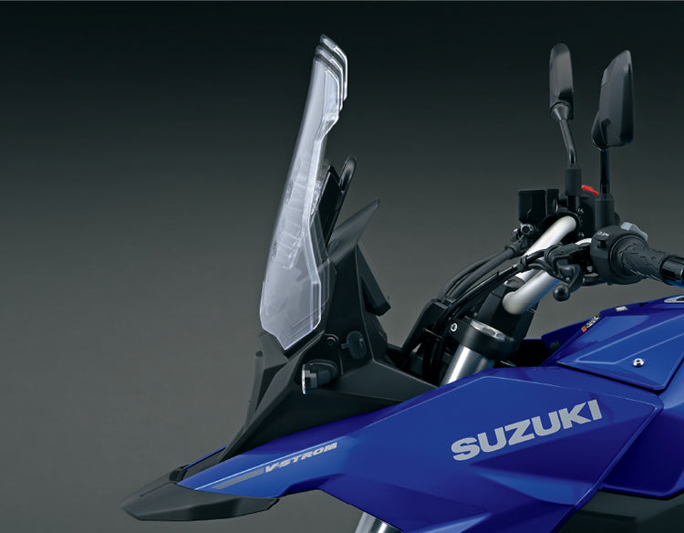 Load image into Gallery viewer, Close-up of a blue Suzuki V-Strom motorcycle showing the clear windshield, handlebars, mirrors, and side fairing against a dark studio background.
