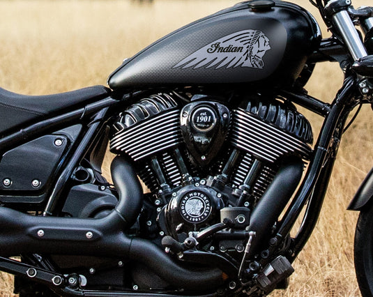 Close-up of a black 2026 Indian Chief Dark Horse motorcycle engine and fuel tank with a white Native American profile logo, photographed outdoors against a dry grassy background.