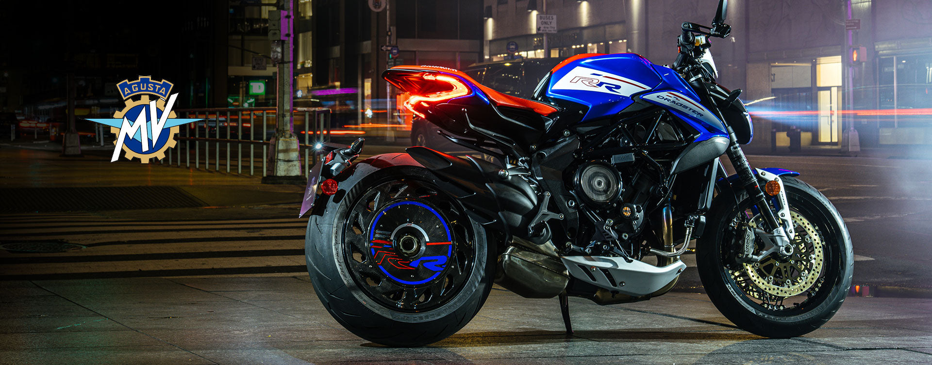 MV Agusta Dragster RR featuring iconic Italian design and triple-exit exhaust, parked on a city street at night with neon lights and MV Agusta logo.