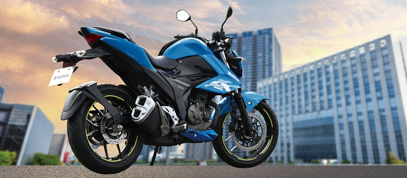 Load image into Gallery viewer, A blue and white 2025 Suzuki GSX 250 LAMS sport motorcycle parked outdoors on a paved surface with blurred modern buildings in the background under a warm sky.
